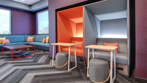 Un espace de détente moderne comprenant un canapé d’angle, deux tables et des poufs.