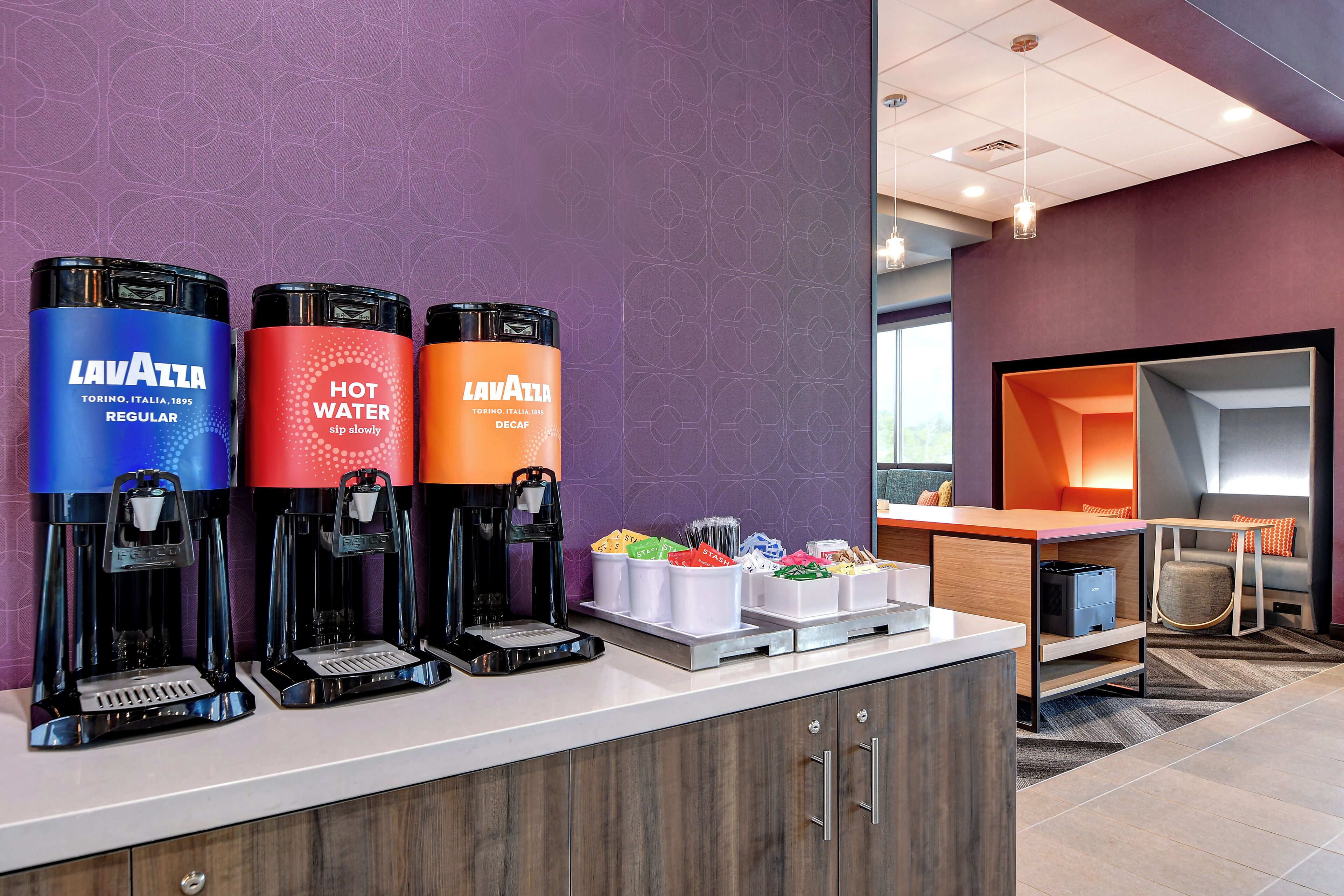 A coffee station with three Lavazza espresso machines, a seating area, and a counter with coffee pods.