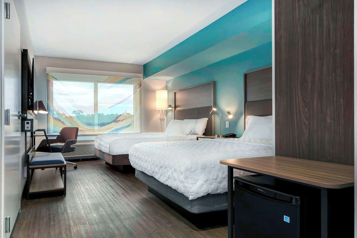 Une chambre d’hôtel avec deux lits, un bureau, une chaise, une télévision et vue sur la plage.