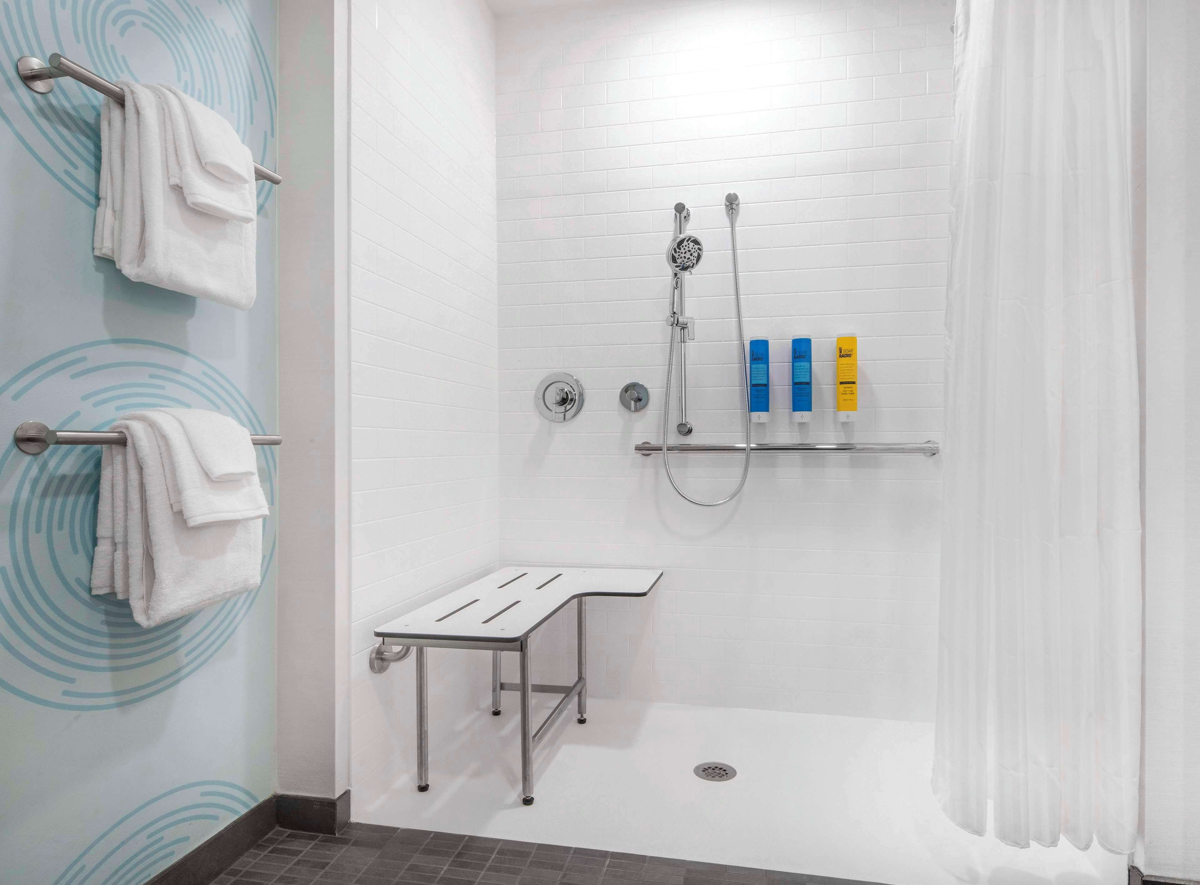Ein zeitgemäßes Duschbad mit Glastür, Handtuchhalter, Duschkopf und Ablagefläche für Toilettenartikel.