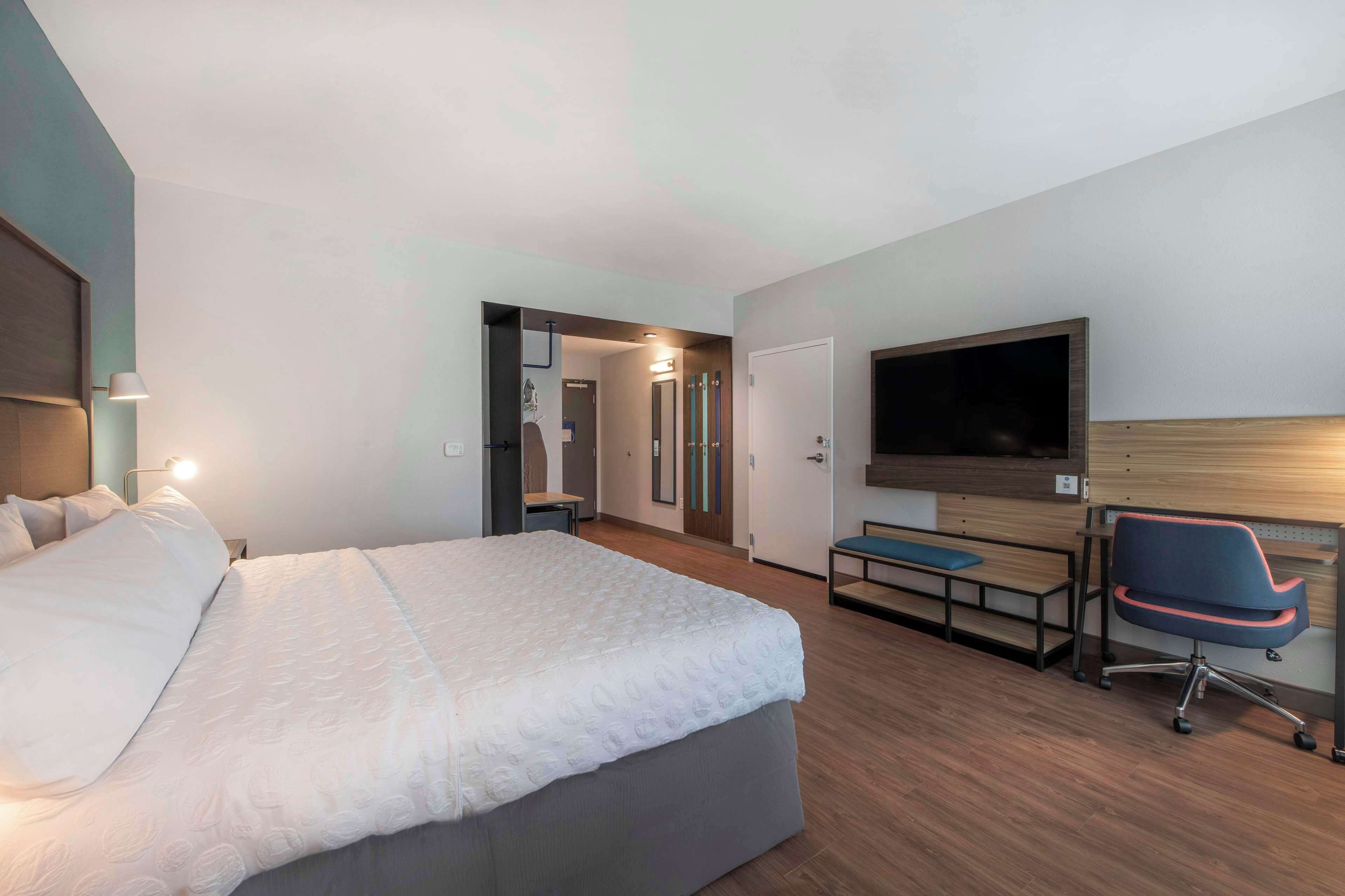 Una habitación de hotel moderna con una cama grande, un escritorio con una silla, un televisor de pantalla plana y un vestidor.