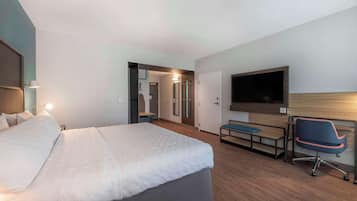 Una habitación de hotel moderna con una cama grande, un escritorio con una silla, un televisor de pantalla plana y un vestidor.