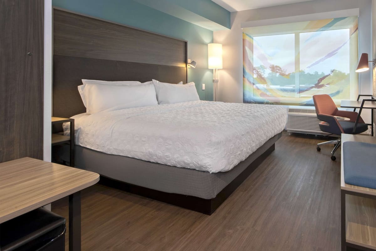 Une chambre d’hôtel avec un grand lit, un bureau avec une chaise, une fenêtre donnant sur un beau paysage et un tableau accroché au mur.