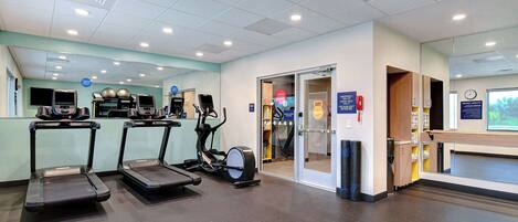 Een sportschool met loopbanden, trainingsfietsen en een spiegelwand.