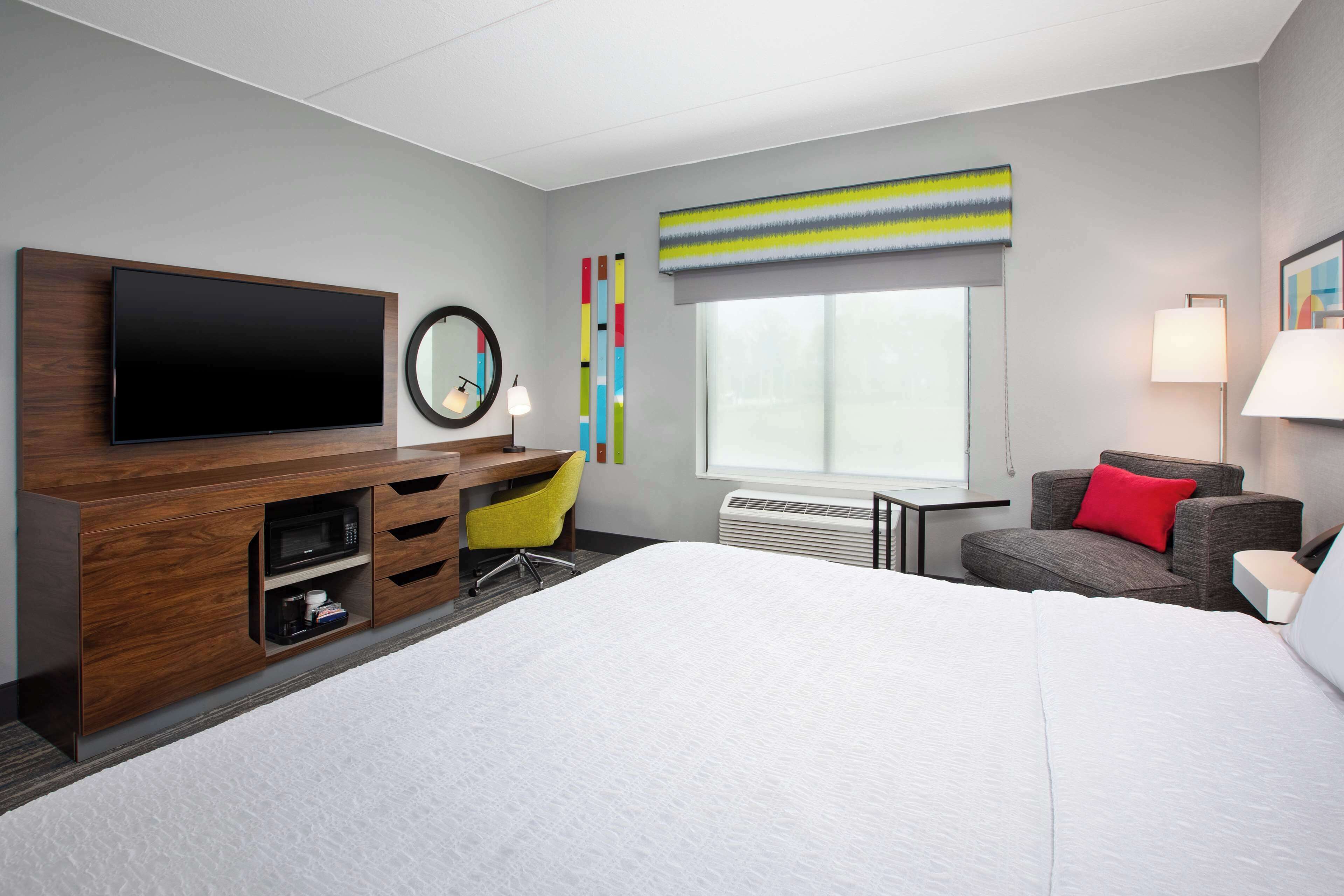 Una habitación de hotel moderna con una cama grande, un televisor de pantalla plana, un escritorio con una silla, un microondas y una ventana con vistas.