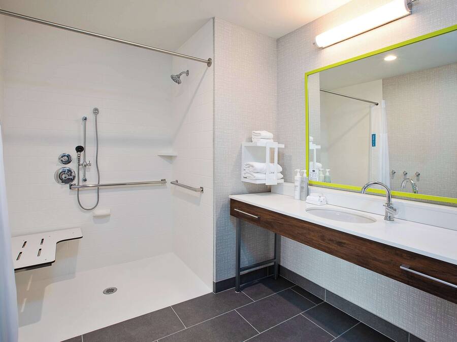 Een moderne badkamer met een inloopdouche, een grote spiegel met groene omlijsting, een witte wastafel en een houten opbergmeubel.