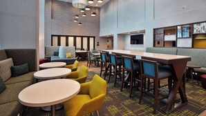 Een moderne lounge met ronde tafels, gele stoelen en een combinatie van zitplaatsen, waaronder banken en zitgedeeltes.