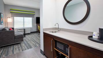 Habitación de hotel con kitchenette, un sofá, un ventanal grande y un espejo redondo.