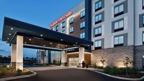 Een moderne hotelentree met een duidelijk bord waarop “Hampton Inn & Suites” staat en een welkomstbord.