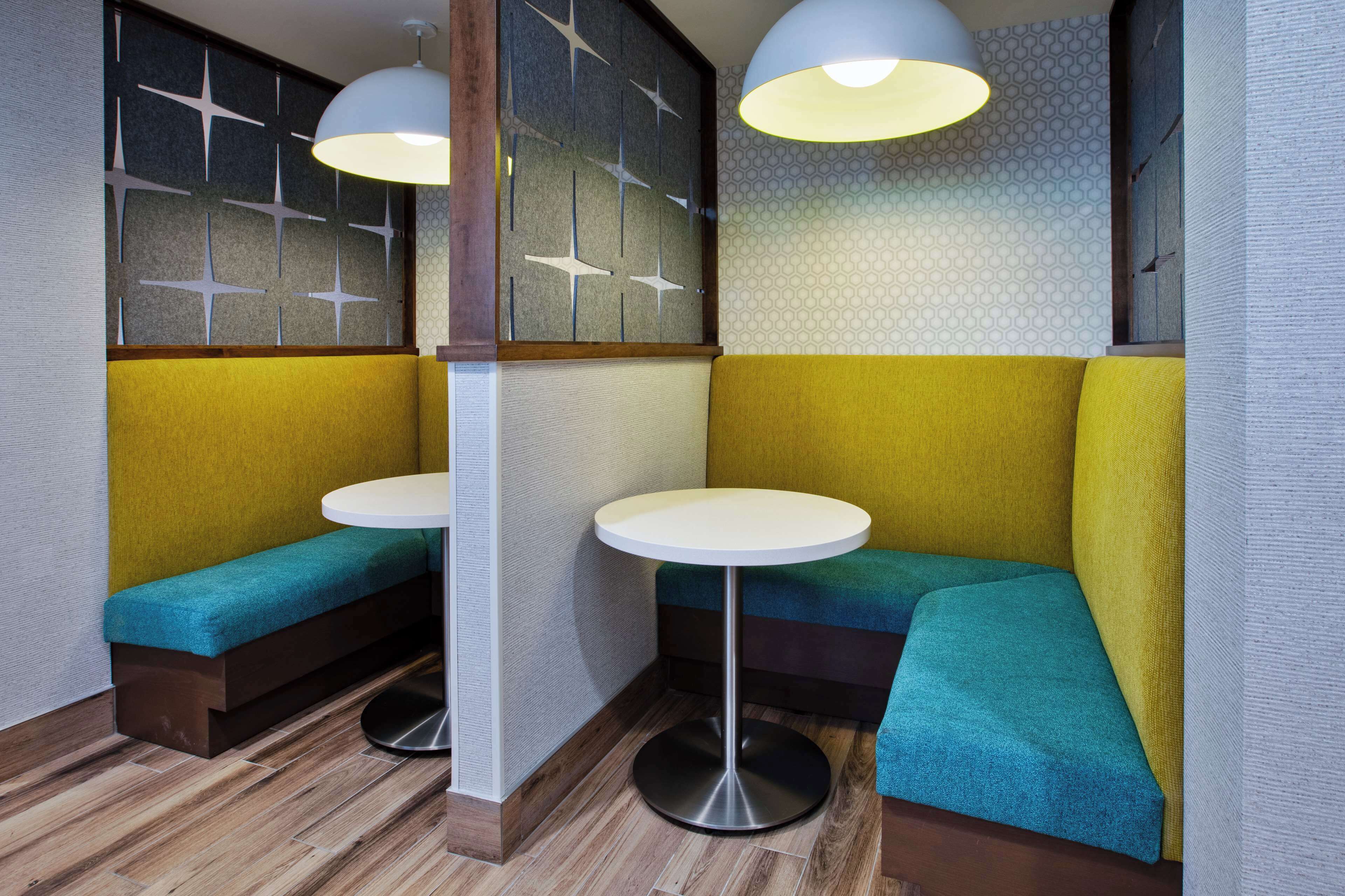 A corner seating area with two round tables and benches, featuring a mix of wooden and upholstered seating.