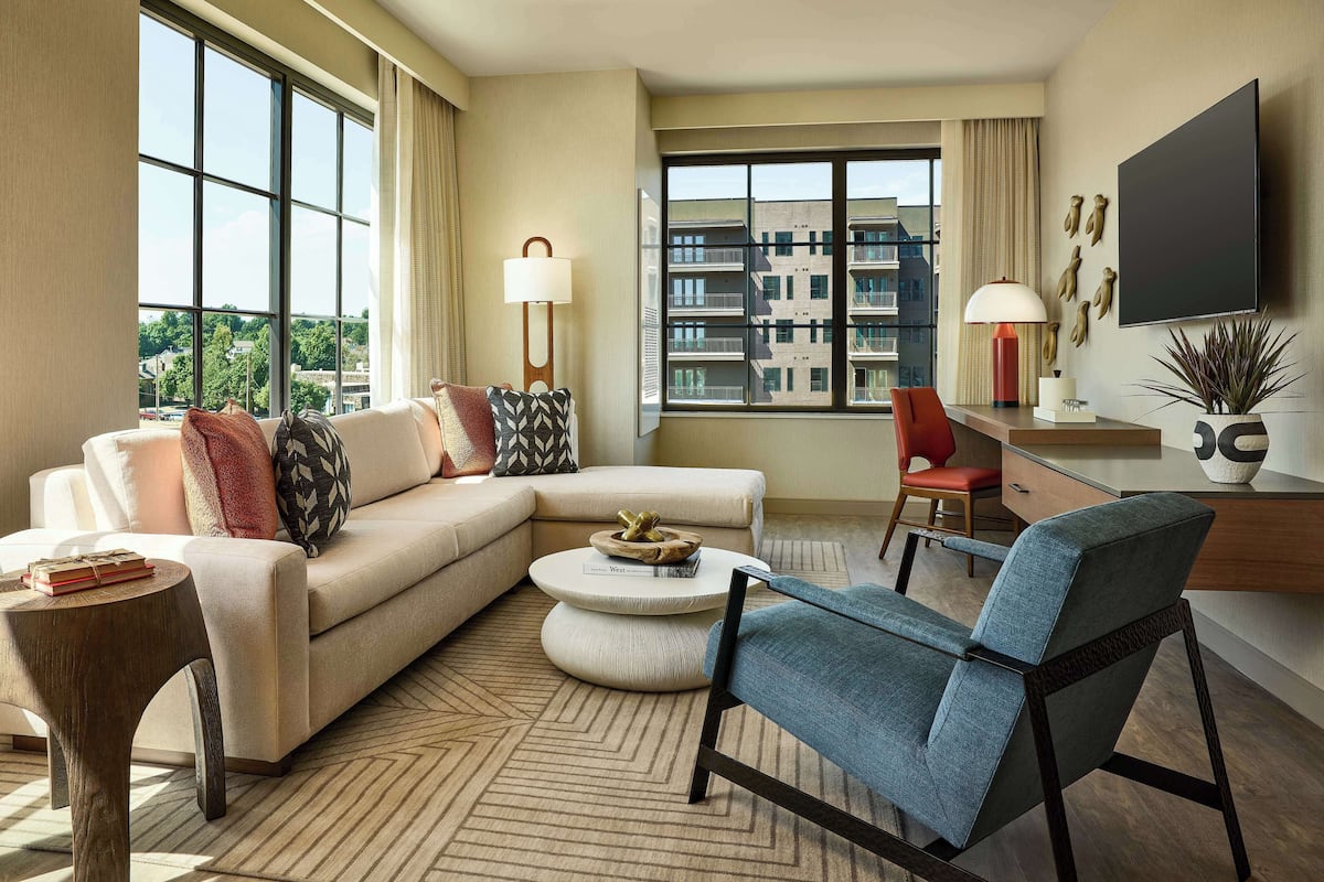 A modern living room with a sofa, armchairs, a coffee table, and a TV mounted on the wall.