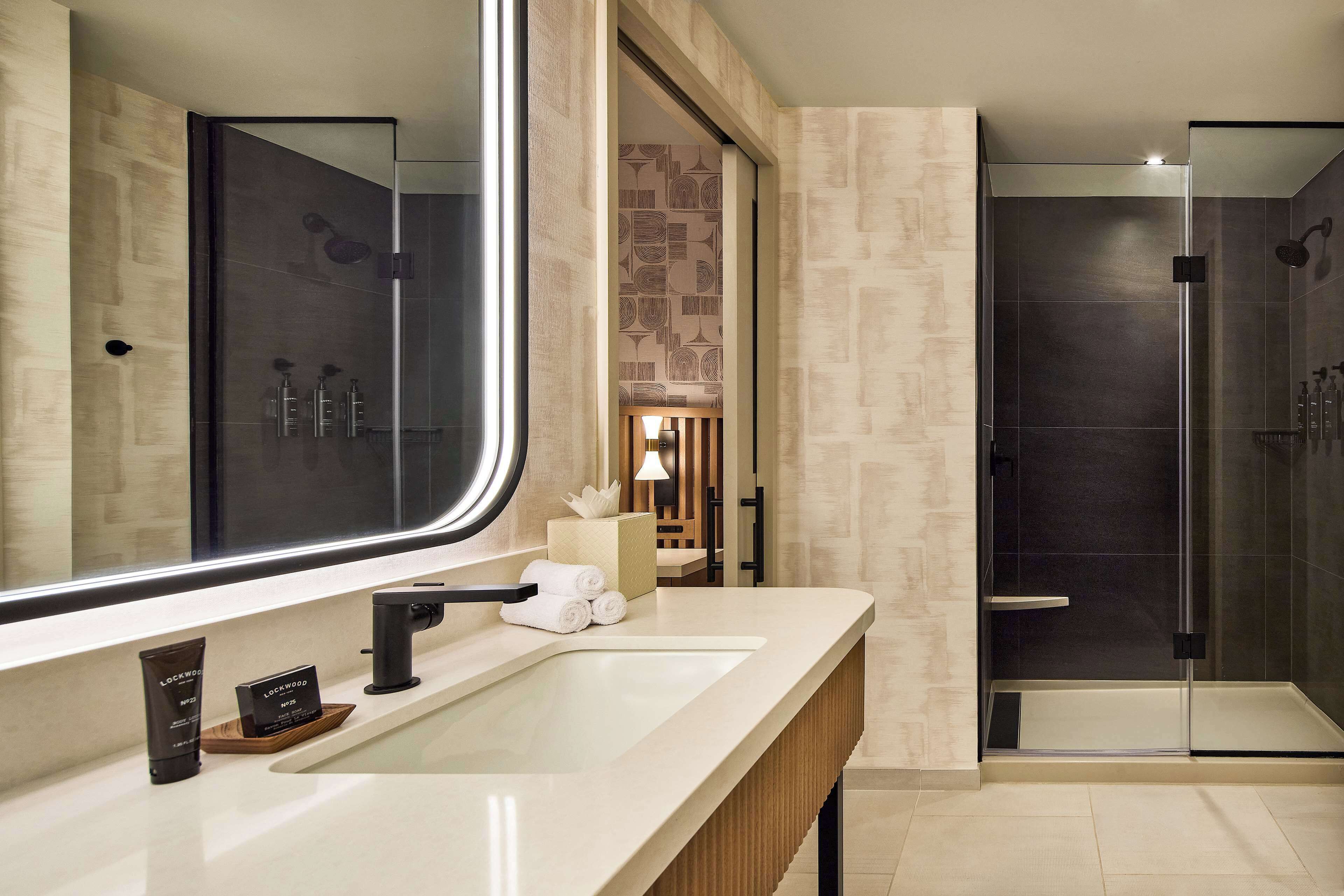 A modern bathroom with a large mirror, a sink, and a shower area.