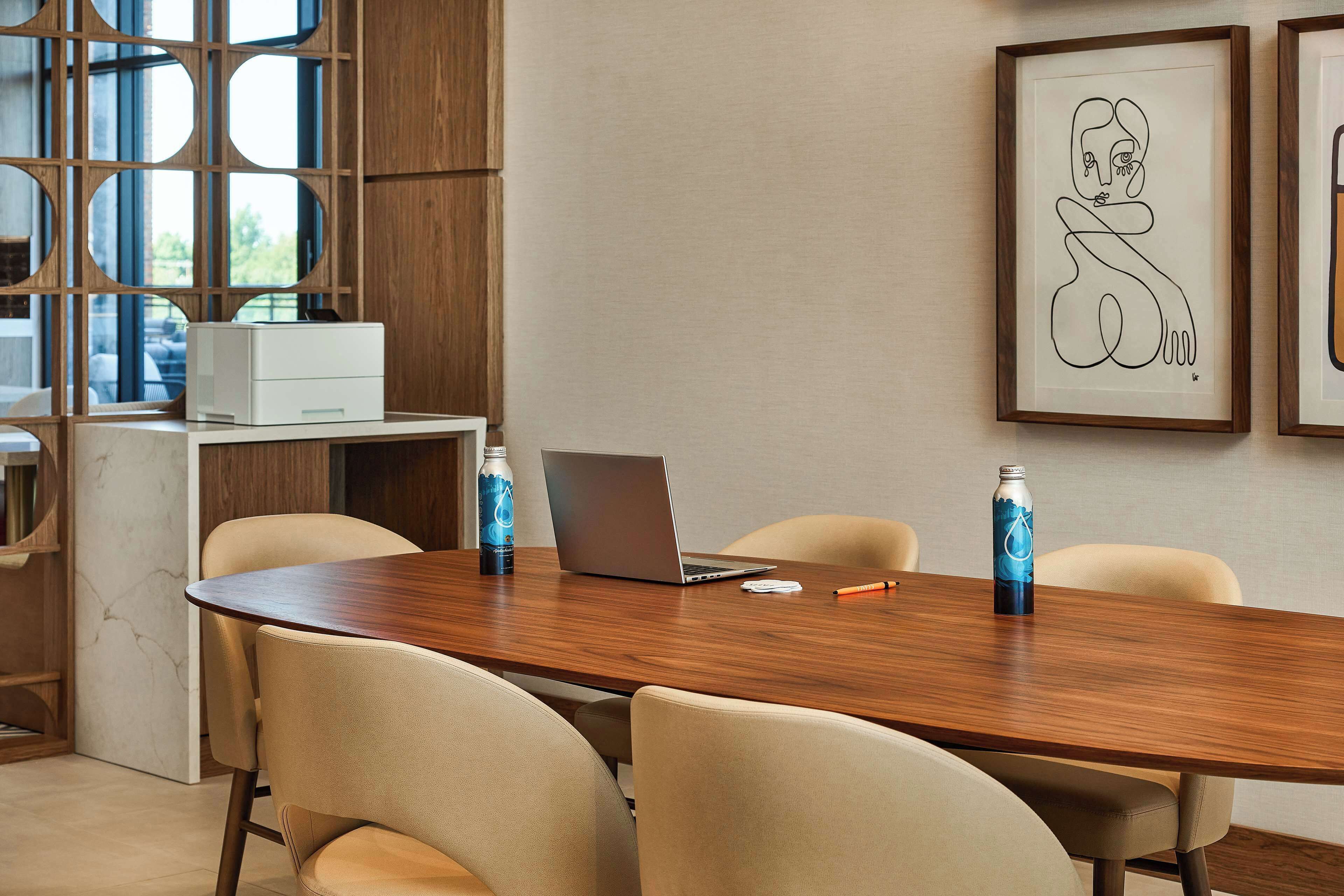 A conference room with a wooden table, four chairs, a laptop, two water bottles, and a framed abstract artwork on the wall.