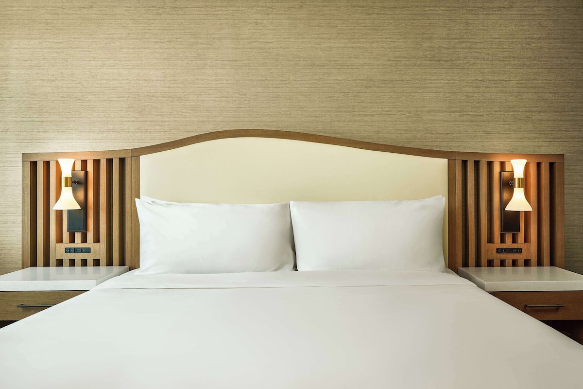 A neatly made bed with white linens, a wooden headboard, and two bedside lamps.