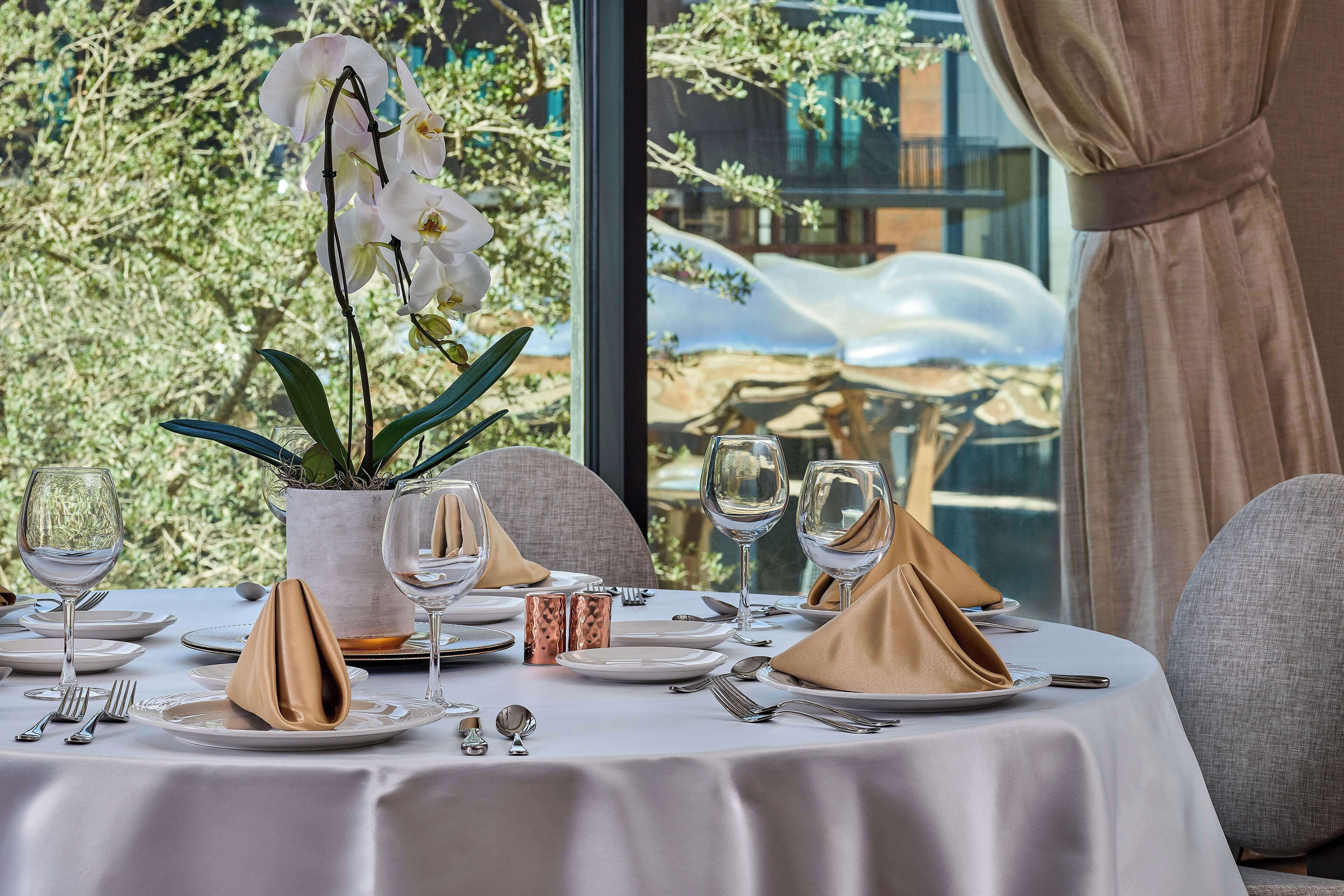 Une table dressée pour un dîner à deux, avec un vase rempli d’orchidées blanches, un verre d’eau et un chandelier.