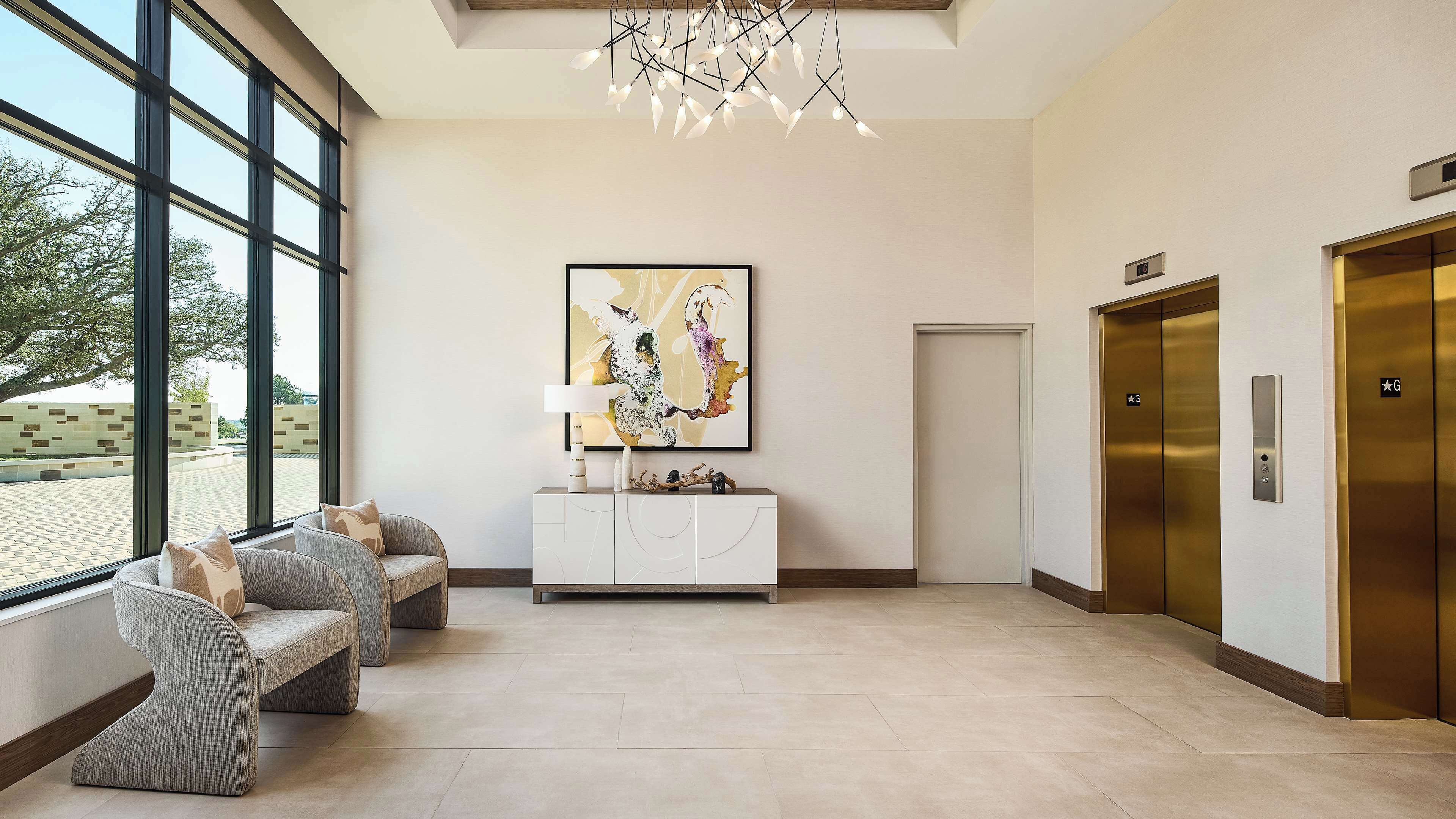 A modern lobby with a large window, a white console table, a colorful abstract painting, and two elevators.