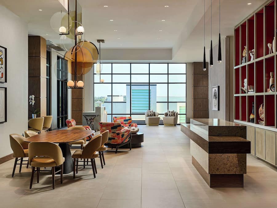 Un comedor amplio con una gran mesa de madera y sillas modernas, una zona de estar con sofás coloridos y un aparador decorativo rojo con varios objetos.