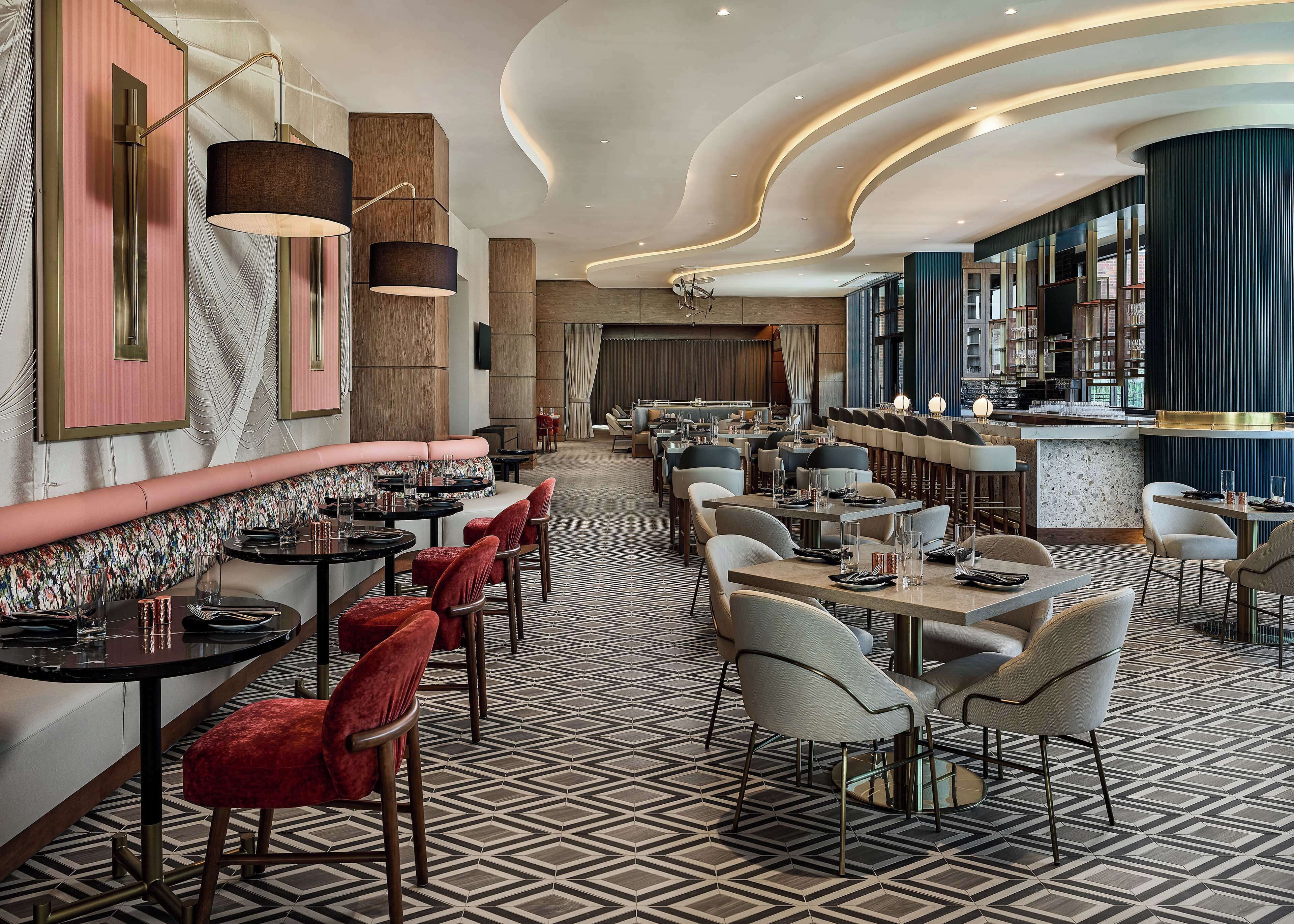 A modern restaurant interior with a central bar, seating arrangements, and a patterned floor.