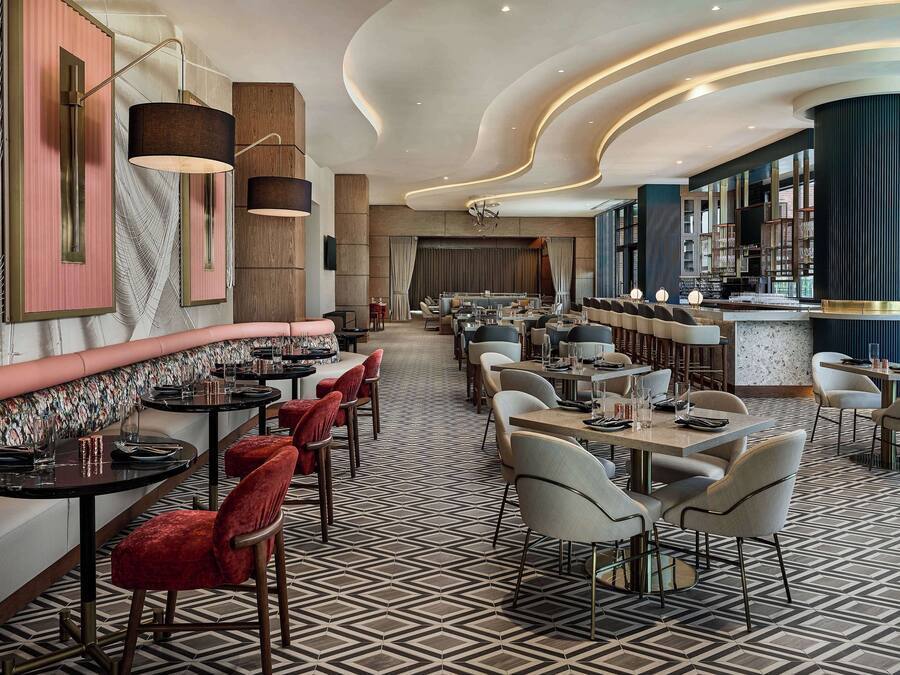 A modern restaurant interior with a central bar, seating arrangements, and a patterned floor.