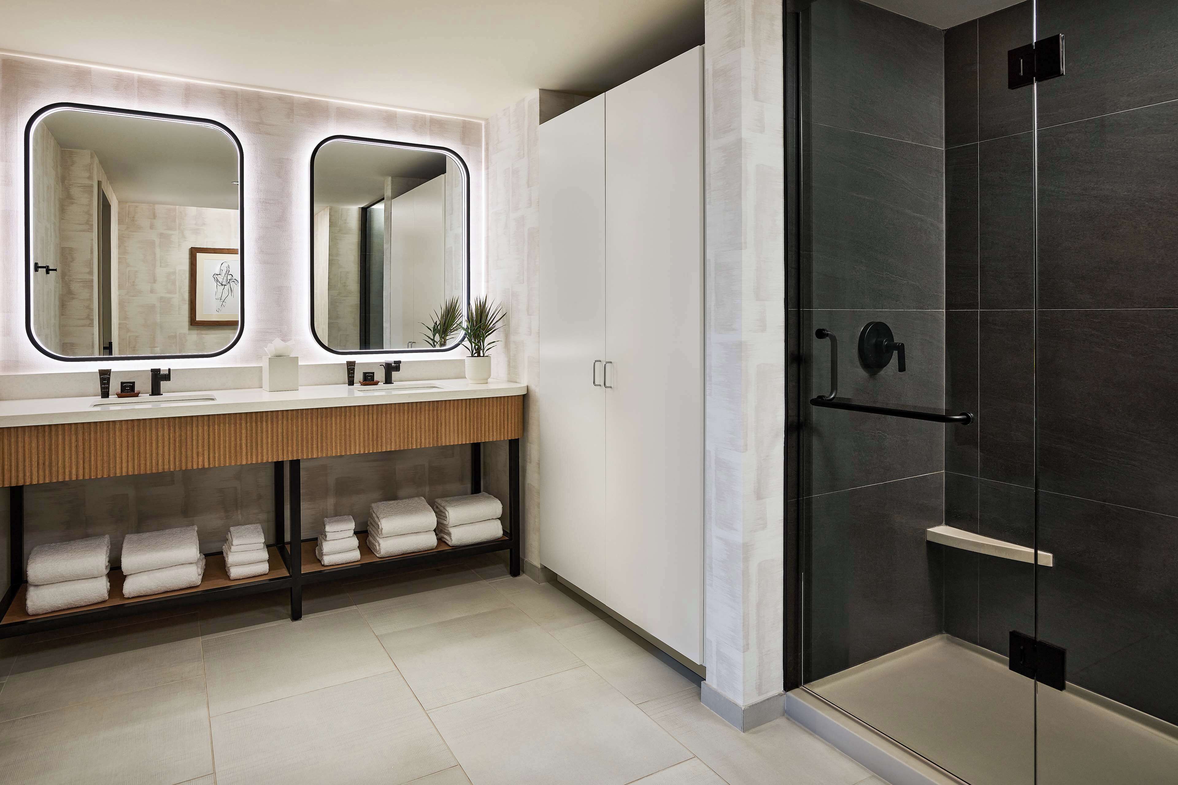 Un baño moderno con tocador doble, cabina de ducha de vidrio y toallas ordenadas en un estante.