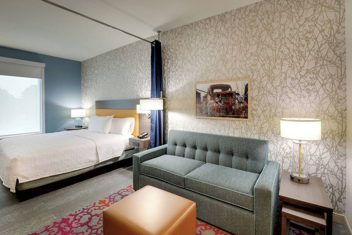 Ett hotellrum med en säng, en soffa, ett litet bord och en lampa.