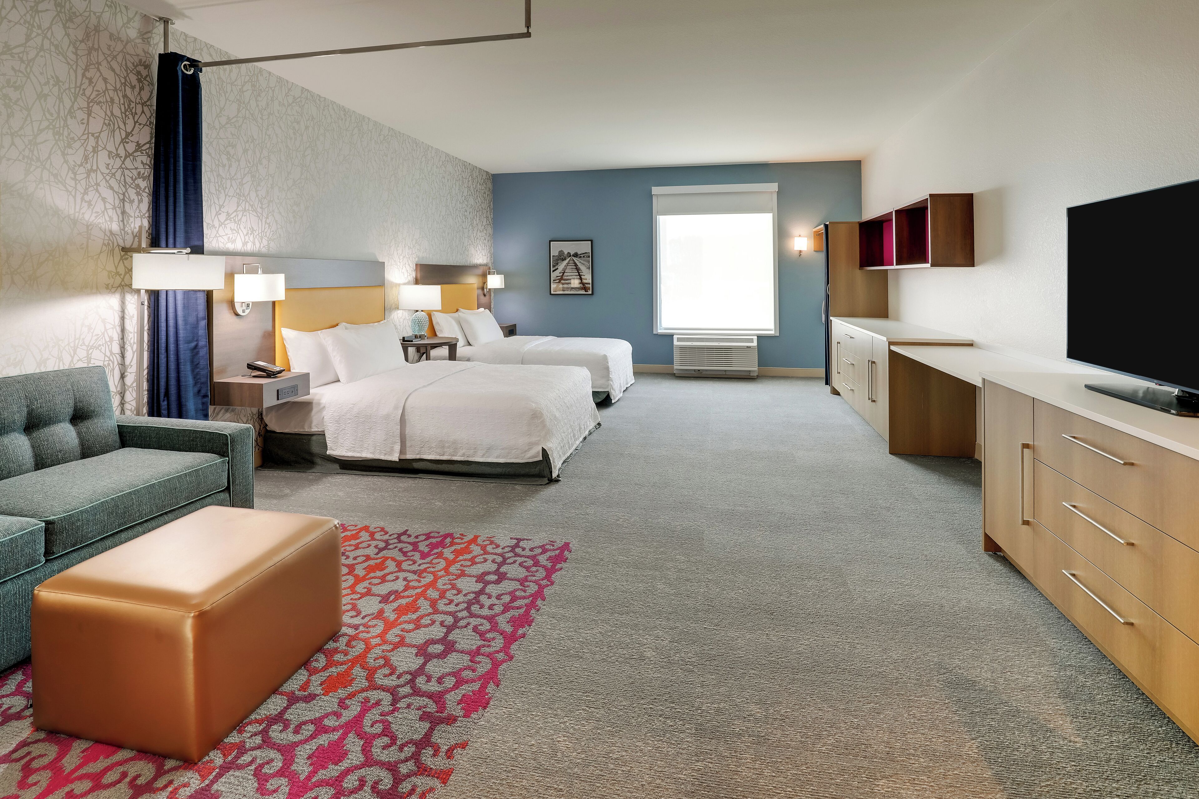A hotel room with a sofa, two beds, a TV, a desk, and a patterned rug.