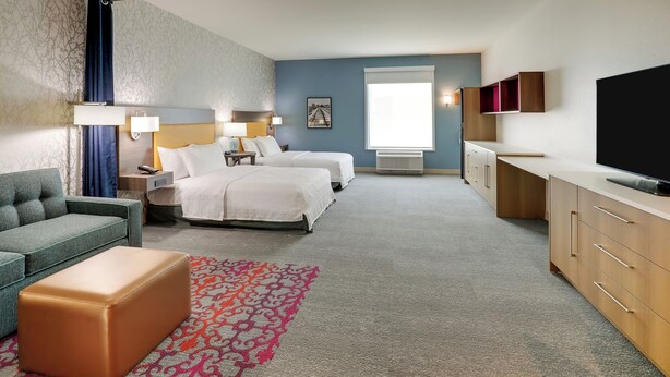 Habitación de hotel con sofá, dos camas, televisión, escritorio y alfombra estampada.