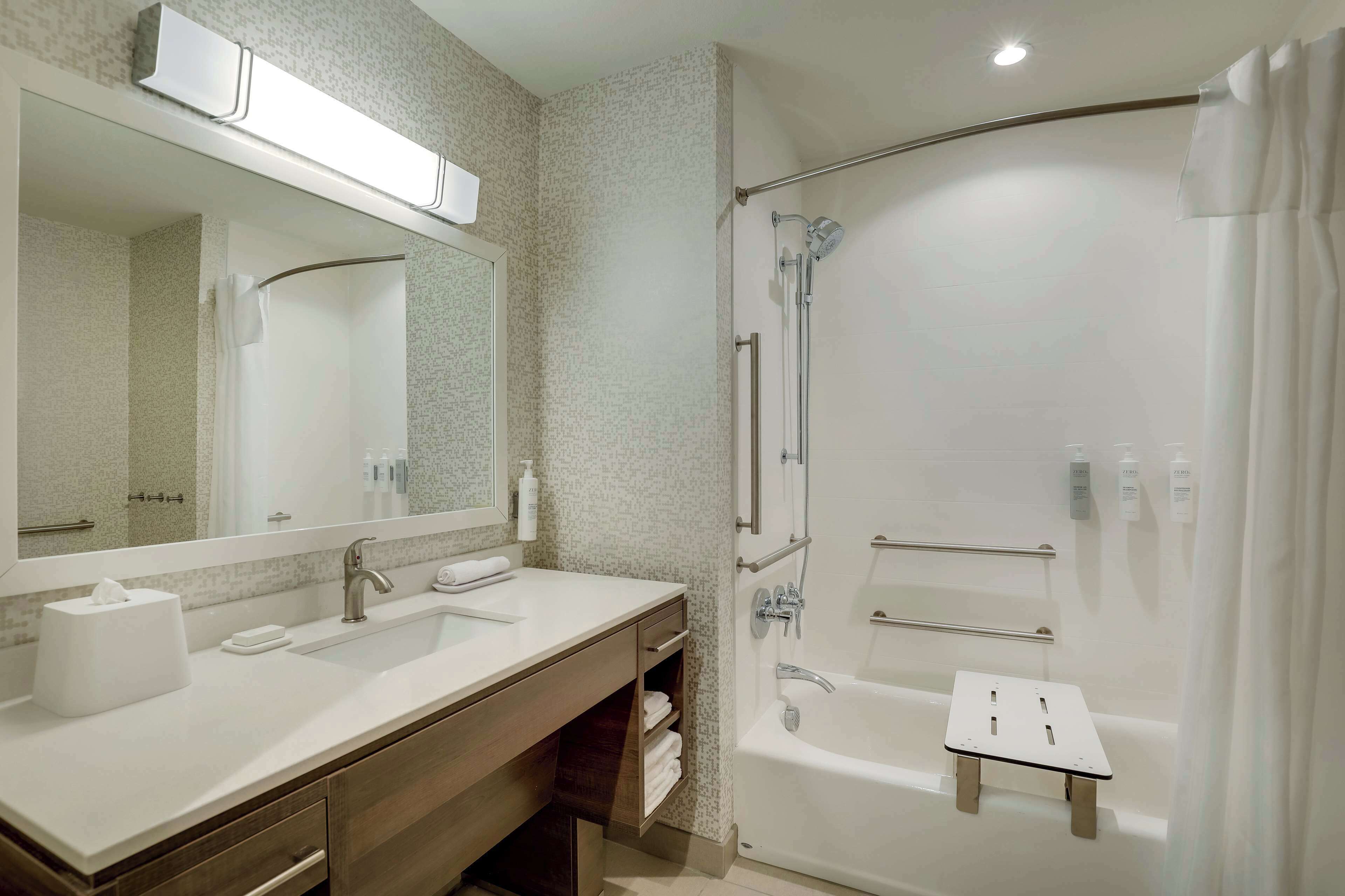 A modern bathroom with a large mirror, a sink, a shower with a glass door, and a bathtub with a small step.