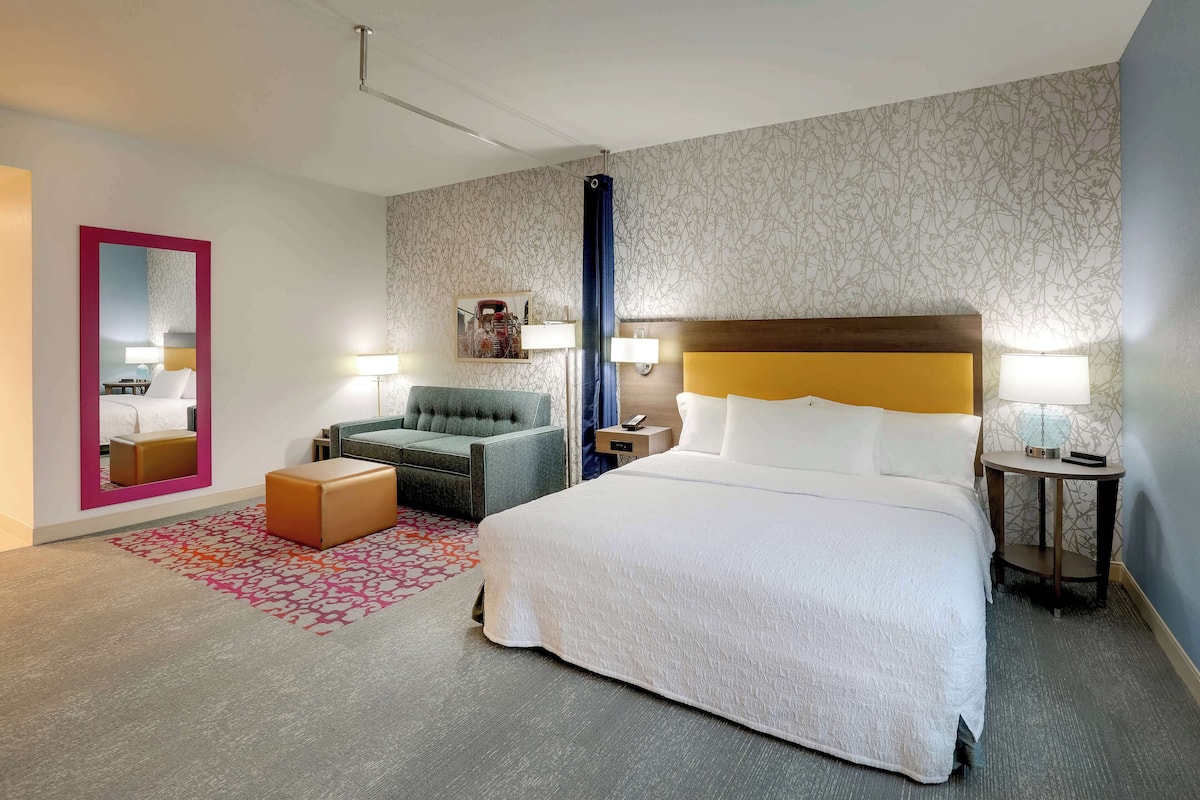 Ett hotellrum med en stor säng, en soffa, en fåtölj, ett litet bord och en spegel.