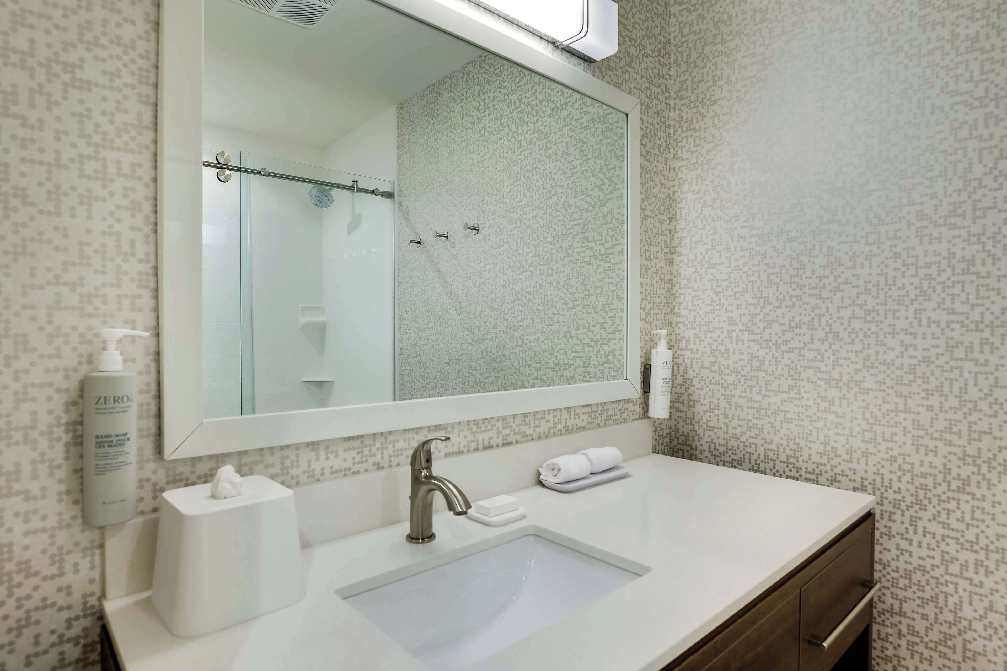 A bathroom with a large mirror, a sink, a towel rack, and a bottle of hand soap.