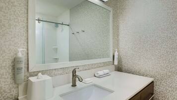 A bathroom with a large mirror, a sink, a towel rack, and a bottle of hand soap.