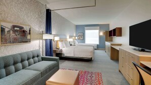 Een hotelkamer met een bed, een slaapbank, een bureau, een televisie en een schilderij aan de muur.