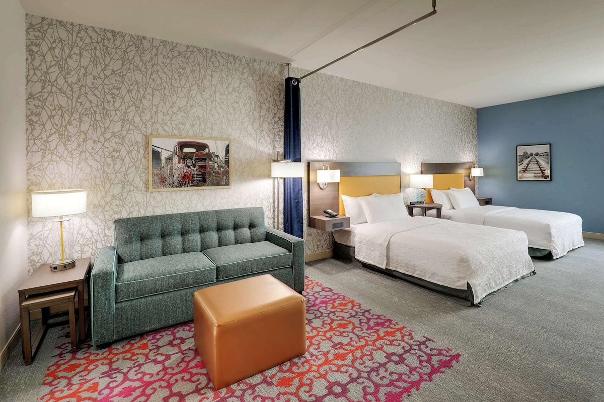 Ett hotellrum med en soffa, två sängar, en mönstrad matta och konstverk på väggarna.