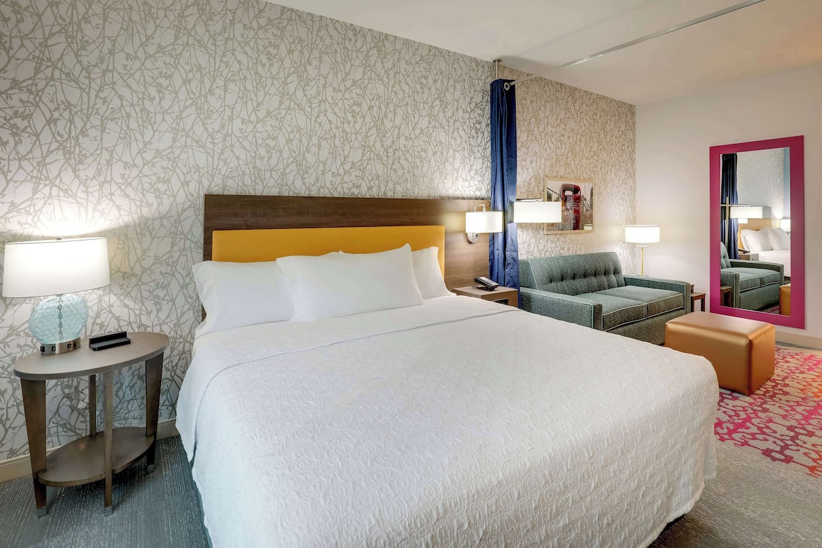 Ett hotellrum med en stor säng, ett sidobord, en soffa, en spegel och en vägg med ett mönster.