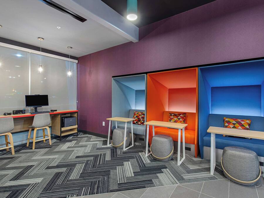 A modern office space with a large window, a desk with a computer, and a seating area with colorful cushions.