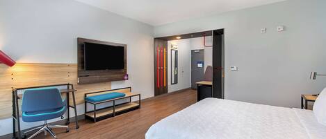 Una habitación de hotel moderna con una cama grande, un escritorio con silla, televisor de pantalla plana y un baño con espejo e inodoro.