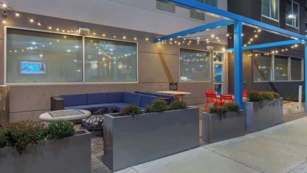 An outdoor seating area with a blue sofa, red chairs, and planters with greenery.
