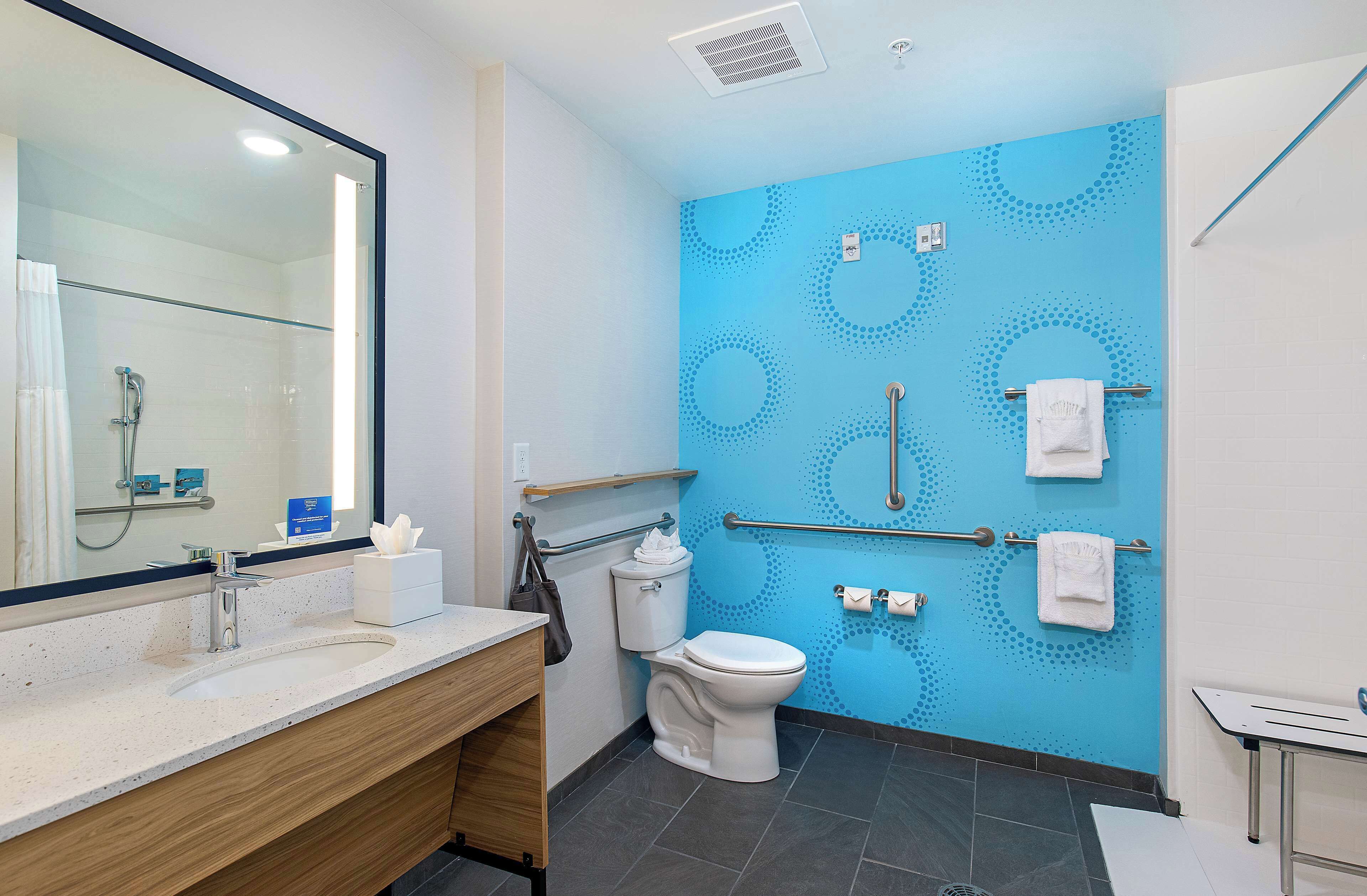 Un baño moderno con pared azul, un espejo grande, un lavamanos, un inodoro y una zona de ducha.