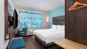 Habitación de hotel con cama, escritorio, silla, televisor y ventana con diseño geométrico.