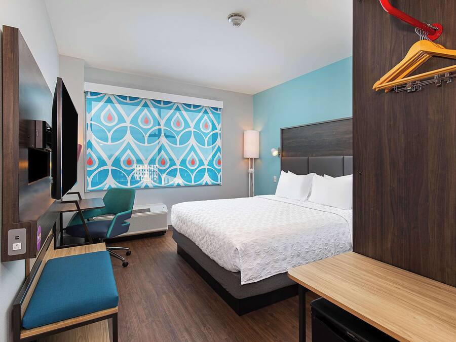 Habitación de hotel con cama, escritorio, silla, televisor y ventana con diseño geométrico.