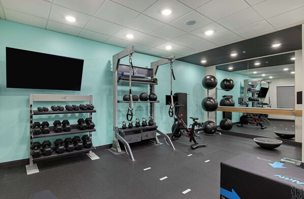 Un gimnasio con equipo de levantamiento de pesas, un televisor en la pared y un espejo que refleja el espacio.