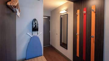 A hotel room with a wooden floor, a blue chair, a shoe rack, and a mirror.