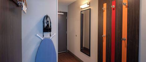 A hotel room with a wooden floor, a blue chair, a shoe rack, and a mirror.