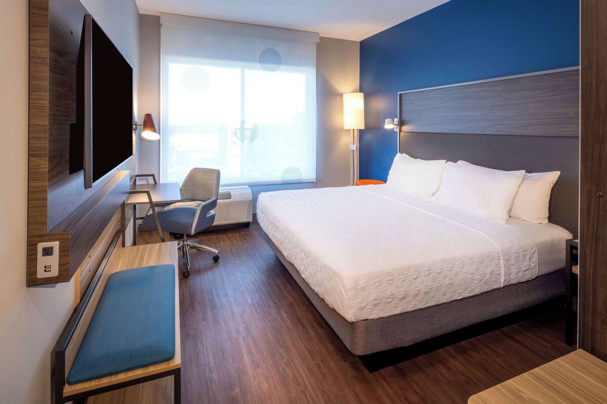 A hotel room with a large bed, a desk, a chair, a TV mounted on the wall, and a window with a view.