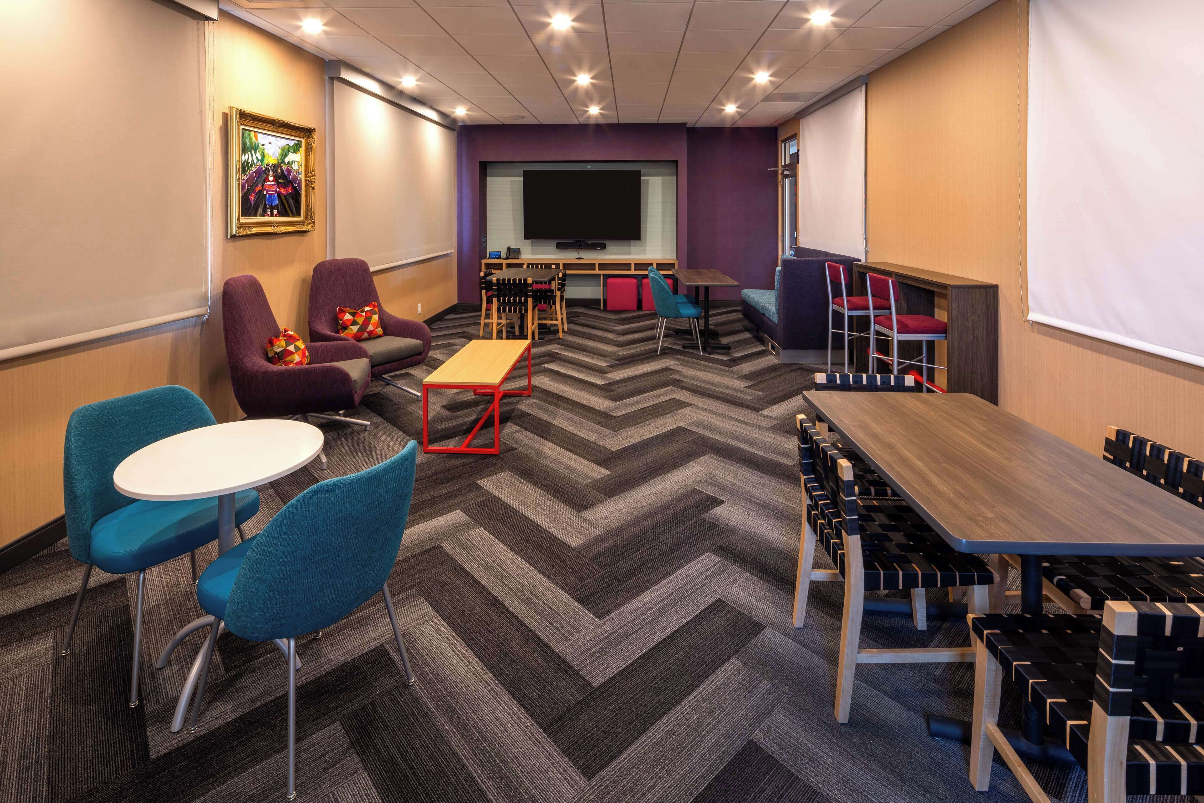 Une salle de conférence dotée d’un grand écran, de plusieurs options d’aménagement pour les sièges et d’un tapis à motifs en chevrons.