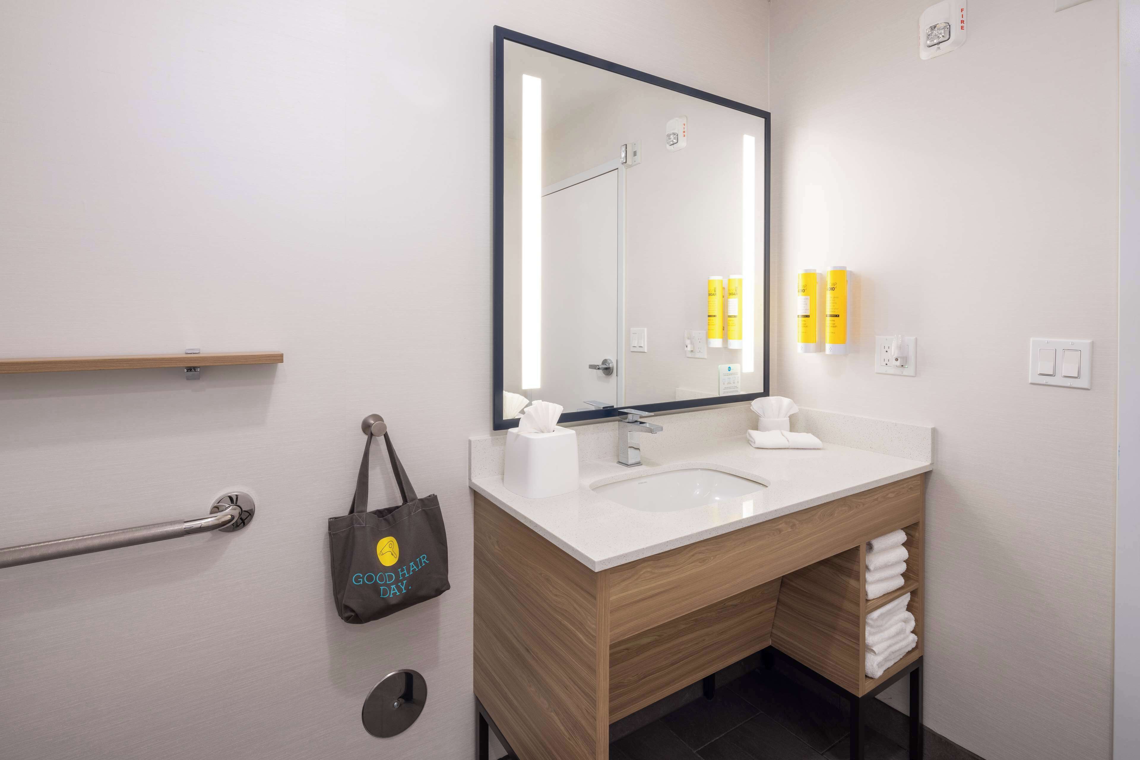 A modern bathroom with a white sink, wooden vanity, a large mirror, and a grab bar.
