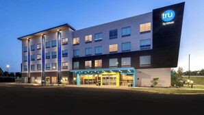 Un hôtel moderne, reconnaissable à son grand panneau « tru by Hilton », qui s’étend sur plusieurs étages et possède une entrée bien éclairée.