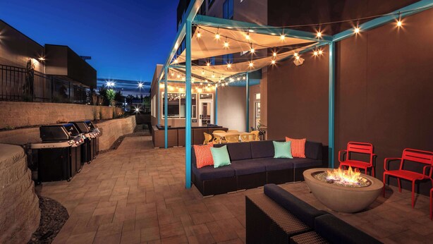 Un espace extérieur aménagé en terrasse, avec un foyer, des sièges et des guirlandes lumineuses.