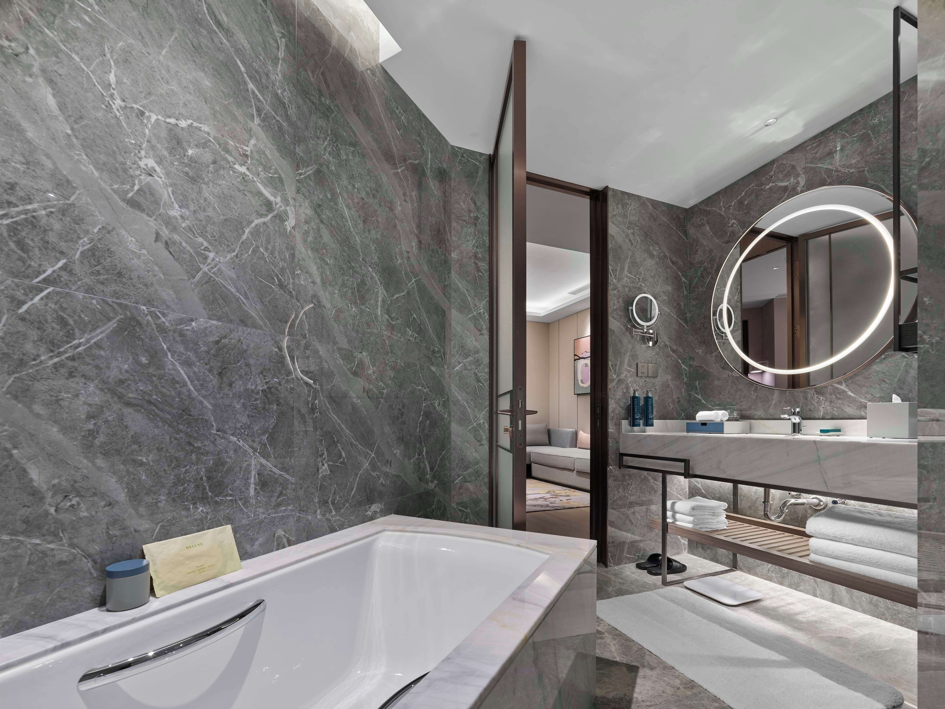 A modern bathroom with a marble wall, a freestanding bathtub, a vanity with a mirror, and a towel rack.