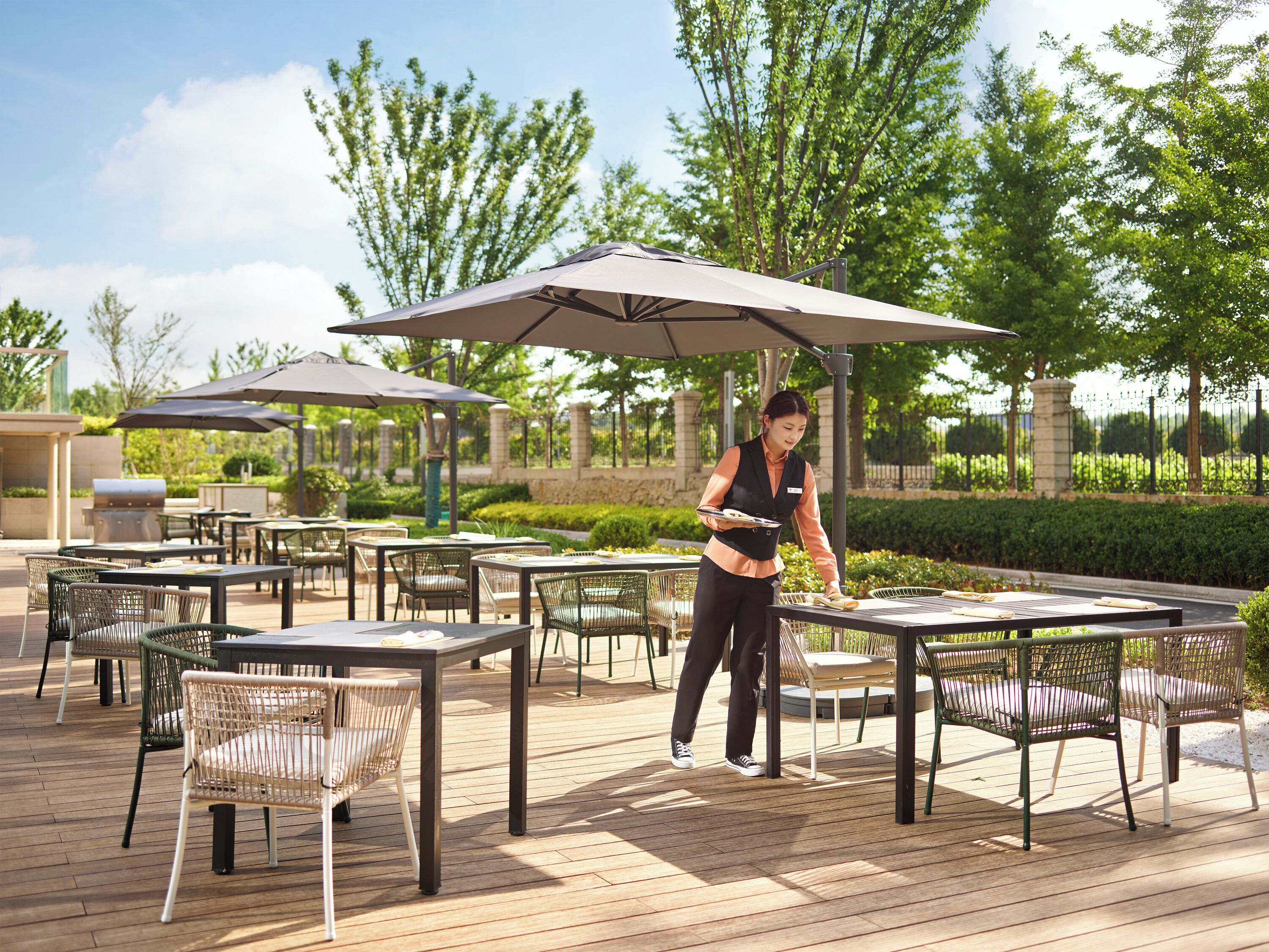 An outdoor dining area with tables and chairs, umbrellas, and a person serving food.